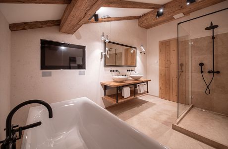 Hier finden Sie genügend Platz im Natursteinbad von der JR Suite Max. Dusche, Badewanne, zwei Waschbecken und mit TV. Separates WC natürlich.