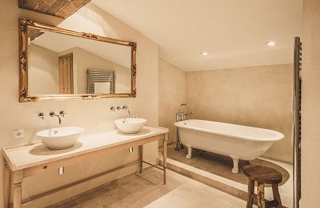 Im Bad der JR Suite Wilder Kaiser finden Sie eine freistehende Badewanne, zwei Waschbecken, viel Platz und alles im Naturstein, kombiniert mit Holz im schicken Stil.